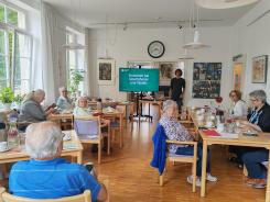 Die Teilnehmenden sitzen im Raum und schauen zur Präsentation auf dem Bildschirm 