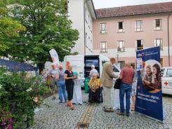 Besucher:innen stehen vor dem Infomobil und an aufgestellten Stehtischen und unterhalten sich