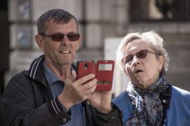 Ein älterer Mann und eine Frau blicken auf ein rotes Smartphone