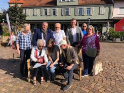 Petra sitzt mit einem älteren Ehepaar auf einer Bank. Hinter ihnen stehen Frau Enders (Seniorenbeirat), der Landrat Schellhaas, Erwin Scharth, Bürgermeister Haus und Herr Scharths Freundin.