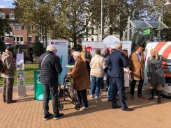 Zwölf Personen stehen vor und neben dem Info-Stand mit dem Info-Mobil und unterhalten sich in verschiedenen Gruppen.