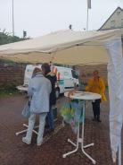 Petra steht mit einer Dame am Info-Stand. Der Info-Stand ist mit einem Pavillon vor dem Regen geschützt.