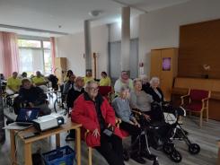 Die Teilnehmenden sitzen auf Stühlen im Raum und blicken zur Leinwand nach Vorne