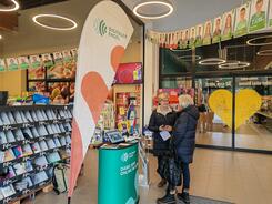 Frau Hernes steht mit einer Besucherin vor dem Infostand im Eingangsbereich des Edeka Marktes