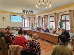 Die Teilnehmenden sitzen an einem großen Tisch im Sitzungssaal und schreiben