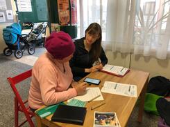 Petra sitzt mit einer Seniorin an einem Tisch. Vor den beiden liegt ein Smartphone.