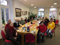 Rund 20 Senior:innen sitzen an einem langen Tisch und blicken gespannt nach vorne.