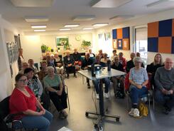 Ein Foto vom Veranstaltungsraum im Senioren- und Pflegestützpunkt Burgdorf. In der Mitte steht ein Beamer. Darum herum sitzen knapp 35 Senior:innen auf Stühlen, die nach vorne blicken.