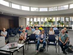 Ungefähr 12 Seniorinnen und 3 Senioren sitzen im Kollegiumssaal im Rathaus Elmshorn auf Stühlen und blicken nach vorne. Im Bild links vorne ist Petras Laptop zu sehen.