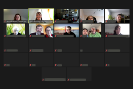 Ein Screenshot einer Zoom-Videokonferenz mit mehreren Teilnehmernden. Oben links sind zwei Moderatorinnen zu sehen, darunter verschiedene Personen, teils allein und teils zu zweit, in ihren Video-Kacheln. Einige Teilnehmer haben ihre Kamera aktiviert und lächeln in die Kamera. Die Namen einiger Teilnehmenden sind anonymisiert oder nicht sichtbar.