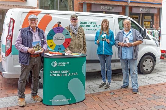 Petra steht mit Peter Aldag, Manfred Grimm und Hein Köhler am Info-Stand vor dem Info-Mobil. Alle vier posieren in die Kamera.