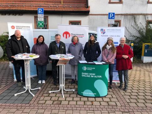 Am Info-Stand gehen gemeinsam sieben Personen der beteiligten Organisationen. In der Mitte steht der Bürgermeister. 