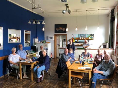 Elf Senior:innen sitzen an zwei Tischen im Kellinghusener Mehrgenerationenhaus. Im Hintergrund stehen Martina und Helmut Priebe an einer Theke.