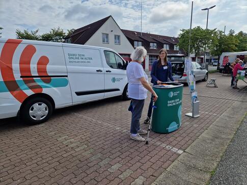 Petra steht mit einer Dame aus Büsum am Info-Stand vor dem Info-Mobil. Die beiden unterhalten sich. 