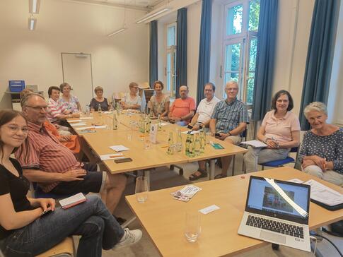 Die Teilnehmenden der Veranstaltung sitzen an einem großen zusammengeschobenen Tisch und blicken nach vorne