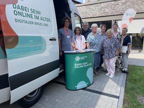 Einige Besucher:innen stehen neben Johannes vor der Infomobil und blicken in die Kamera