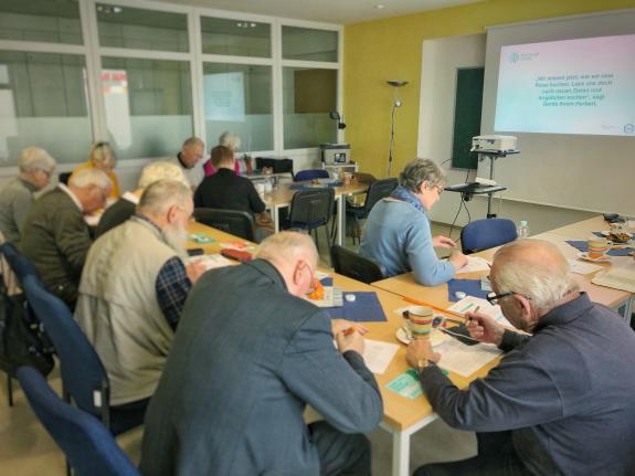 Eine Gruppe von Senioren sitzt am Tisch und macht sich Notizen